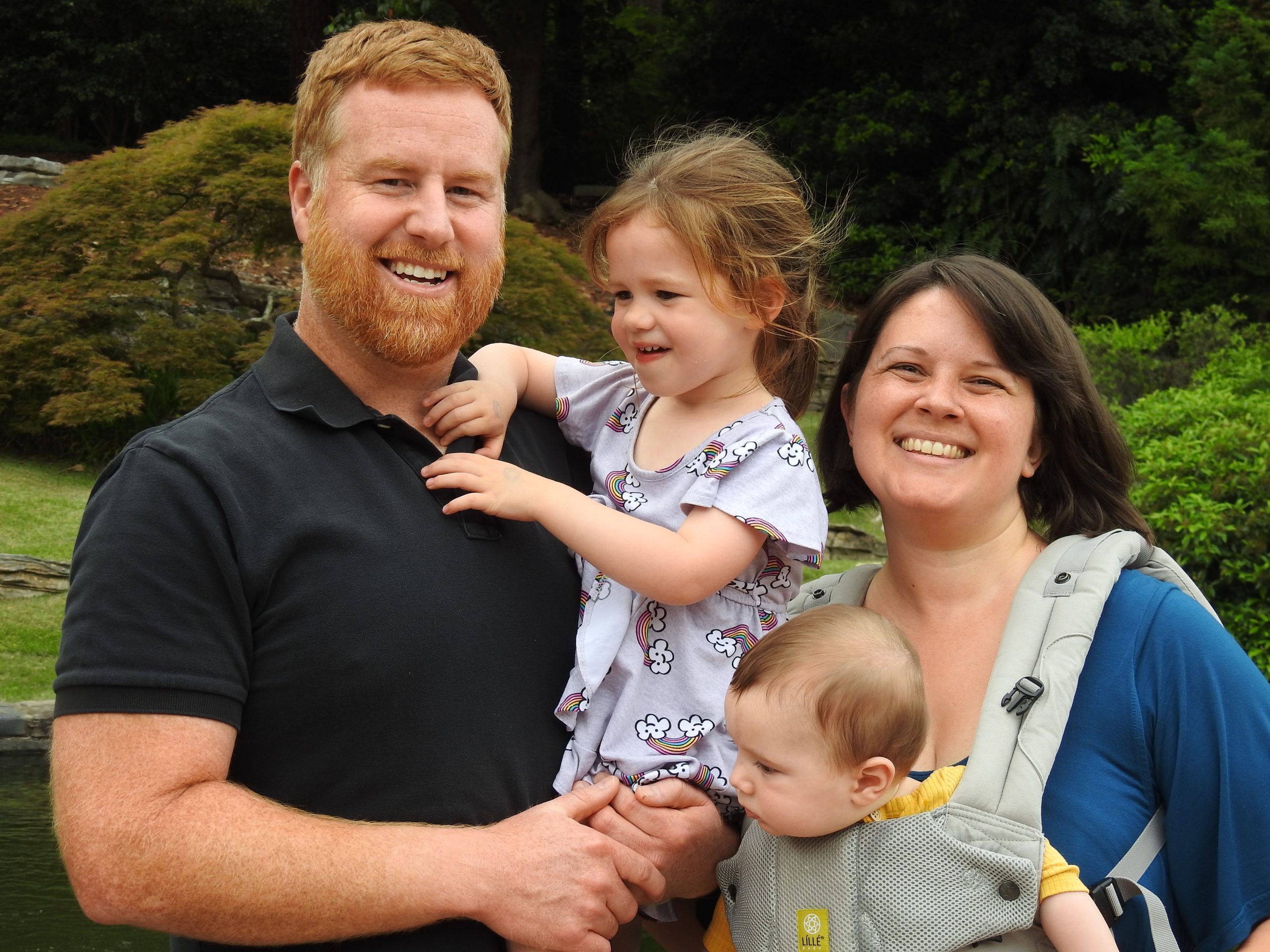 A family of four in a garden, the baby in a front carrier