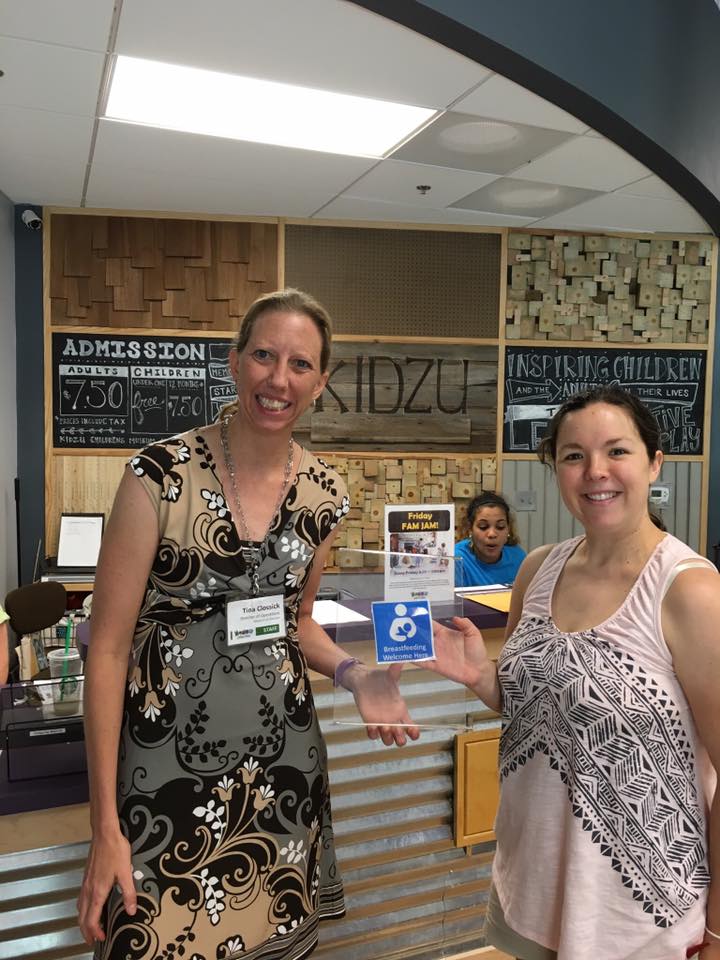 Two women are smiling into the camera while showing the Breastfeeding Welcome Here cling.